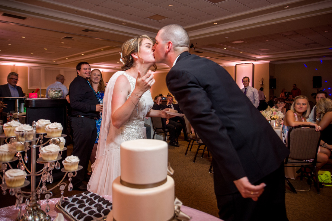 Picture of bride and groom in a ballroom, sharing a kiss after cutting their wedding cake