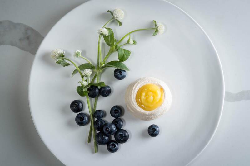 Lemon meringue filled with lemon curd, on a plate with blueberries and white flower stems