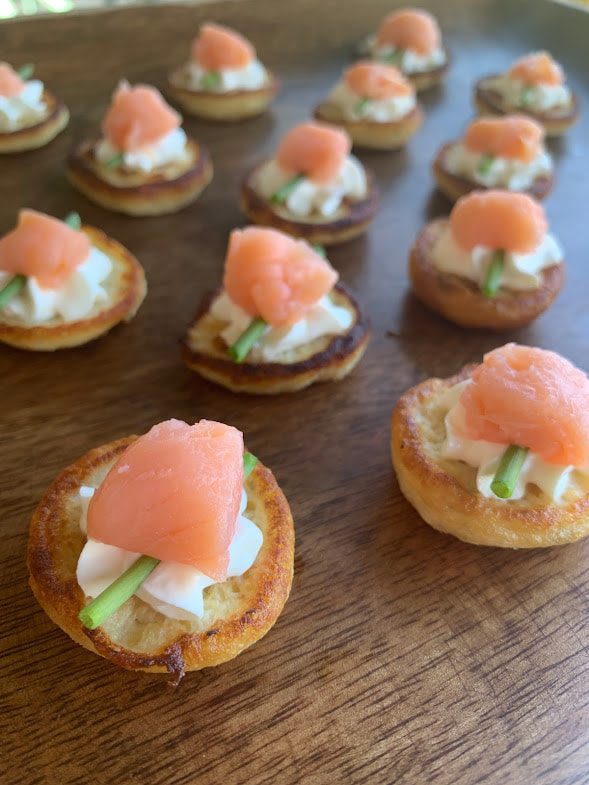 Close up picture of smoked salmon canapes: potato pancake topped with sour cream, chive and smoked salmon on a wooden board